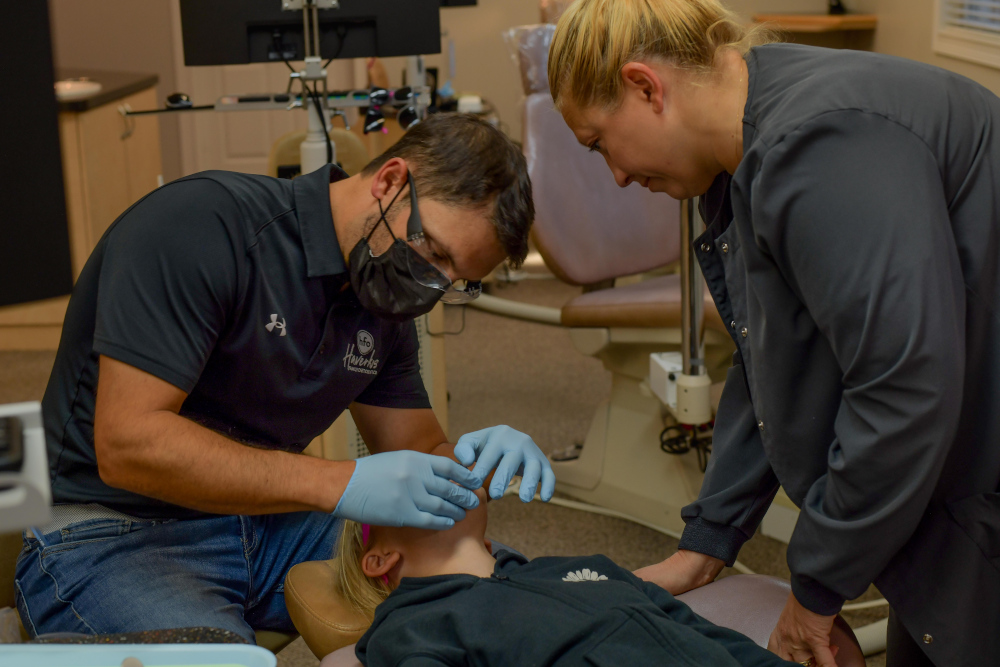Orthodontist treating a young patient in the dental chair with an assistant nearby.