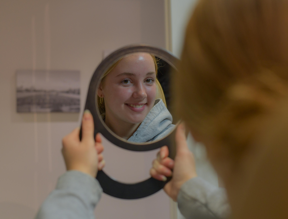 Young patient in the dental chair looking at her smile results through a mirror.