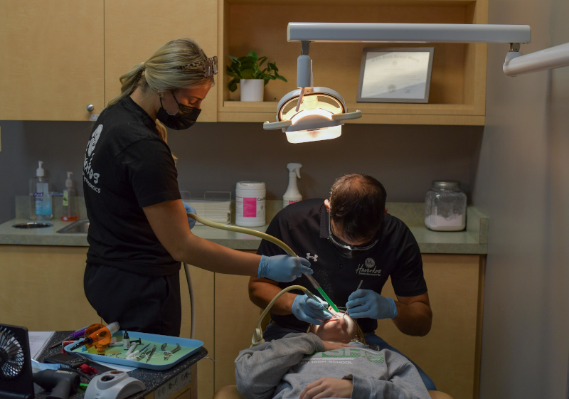 Orthodontist treating a young patient in the dental chair with an assistant nearby.